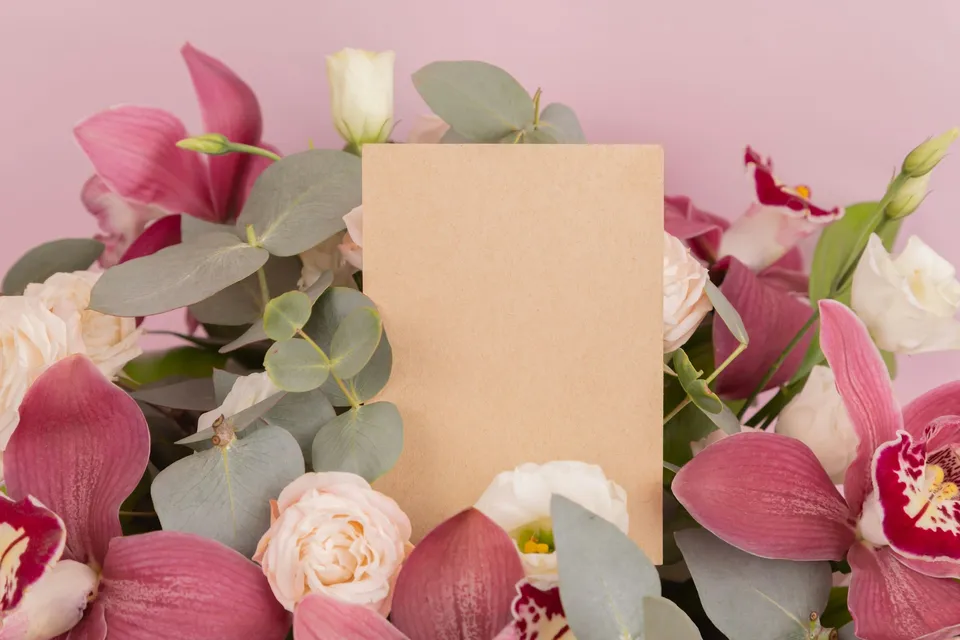 Una tarjeta de papel kraft en blanco entre rosas, orquídeas y ramas de eucalipto