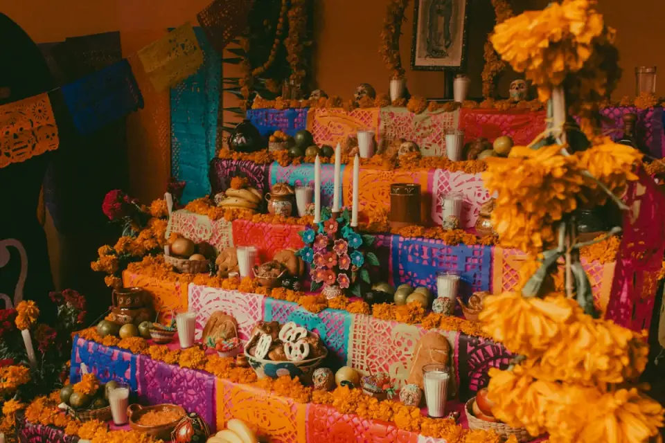 A multi-level ofrenda with colorful papel picado, candles, sugar skulls, bread, fruit and orange marigolds