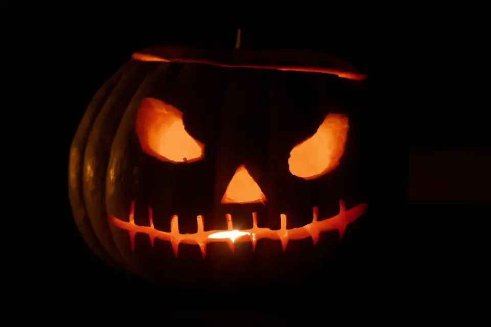 A carved jack-o'-lantern glowing orange in the dark, with angry eyes and a toothy grin