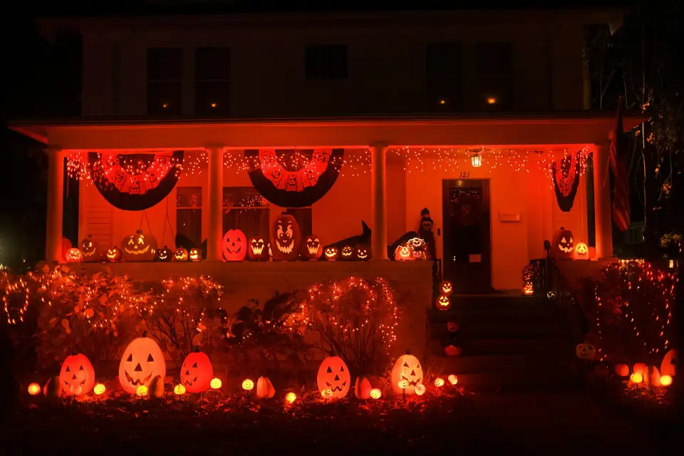 A house at night with its porch lit in orange and dozens of glowing jack-o'-lanterns on the steps and in the yard