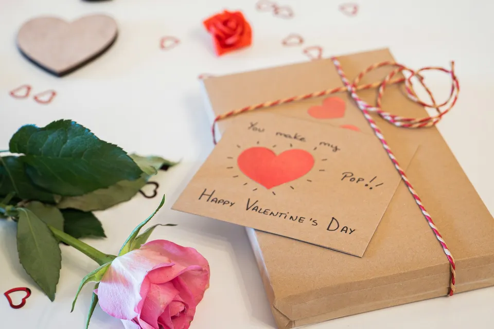 A Valentine's card, a rose and heart confetti on a table