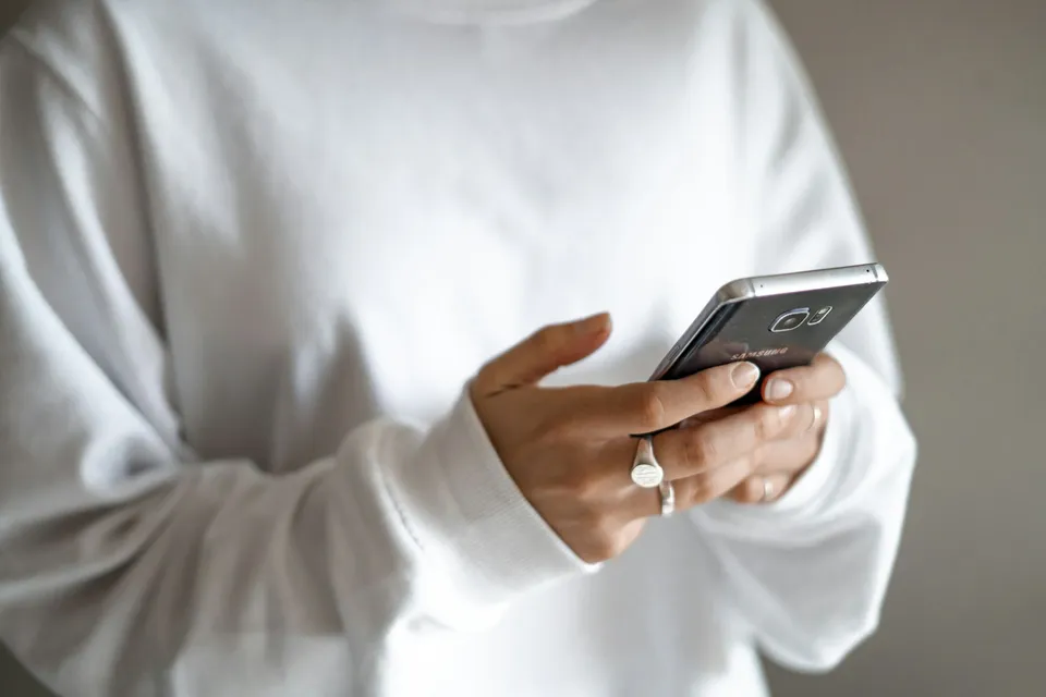 Hands in a white sweater typing a message on a phone
