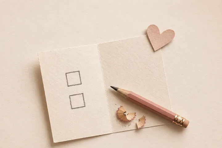 A note with two empty tick boxes, a pink pencil and a paper heart